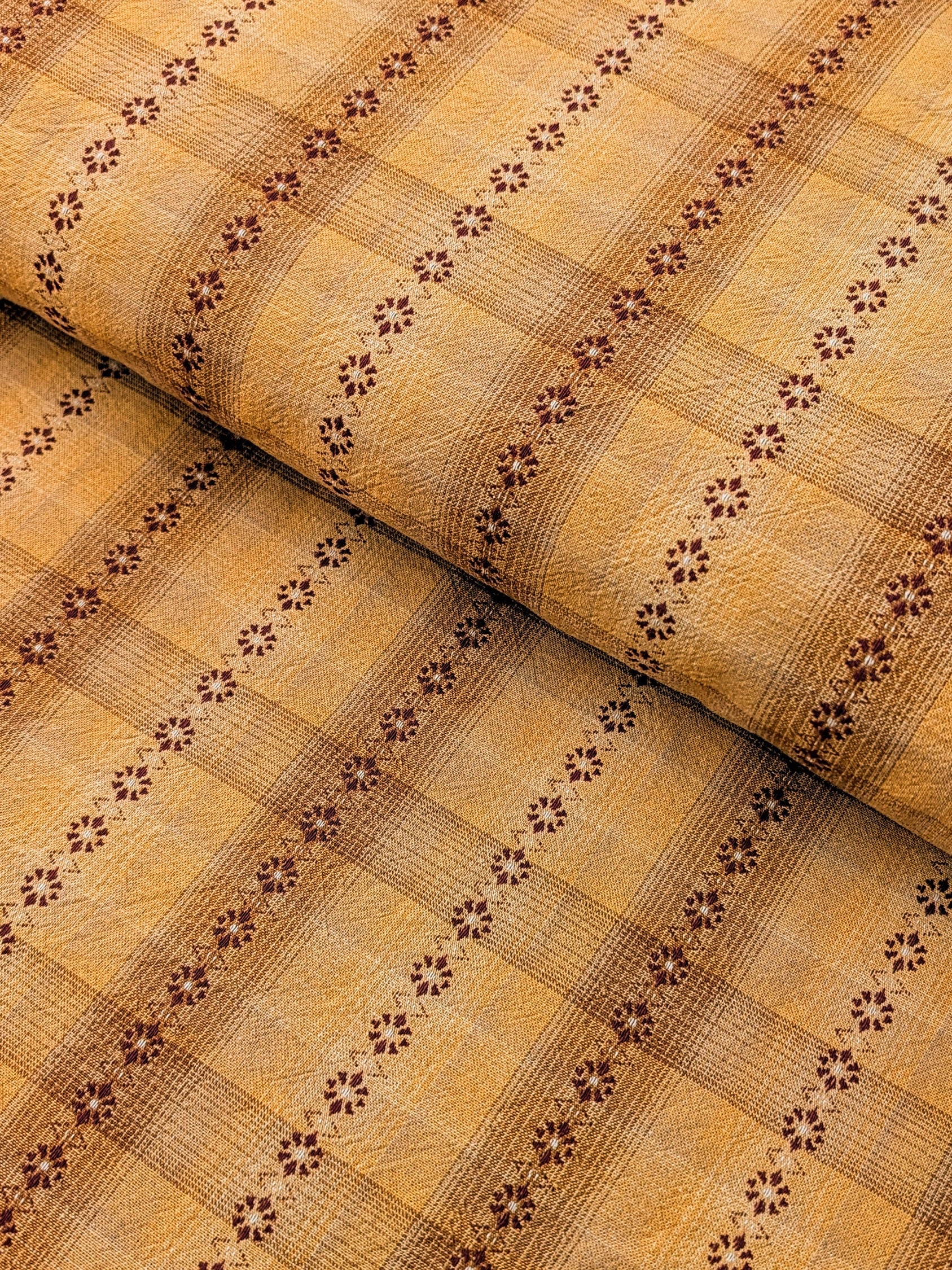 Textured woven fabric with flower-shaped brown pattern on a yellow background